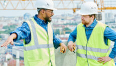 Two people wearing safety vests and hard hats discussing something on a construction site.