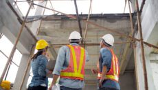 Three people on a jobsite wearing hard hats and hi-vis safety vests looking up at a structure under construction.