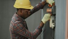 Man wearing hard hat and safety gloves working on electrical wiring.