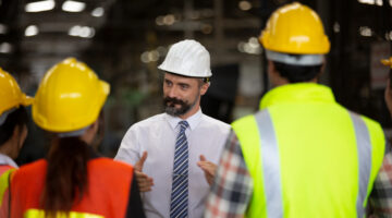 Staff member in hard hat leading a meeting in an industrial setting.