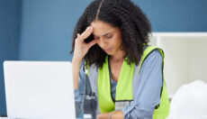 Stressed worker in hi-vis safety vest touching her forehead and closing her eyes.