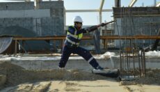 Construction worker in safety vest, hard hat, safety glasses, and gloves using a tool to bend rebar.