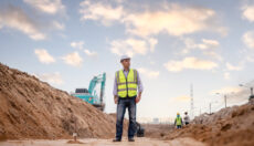 Supervisor on construction site wearing yellow safety vest and white hardhat.